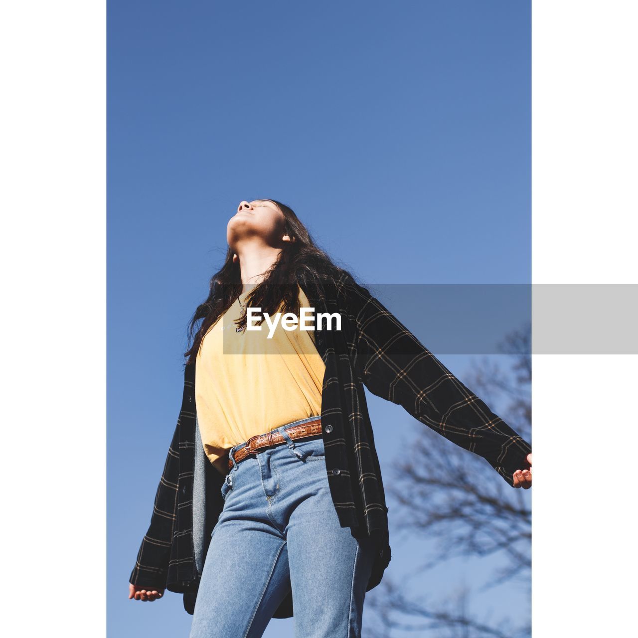 Low angle view of woman standing against clear blue sky