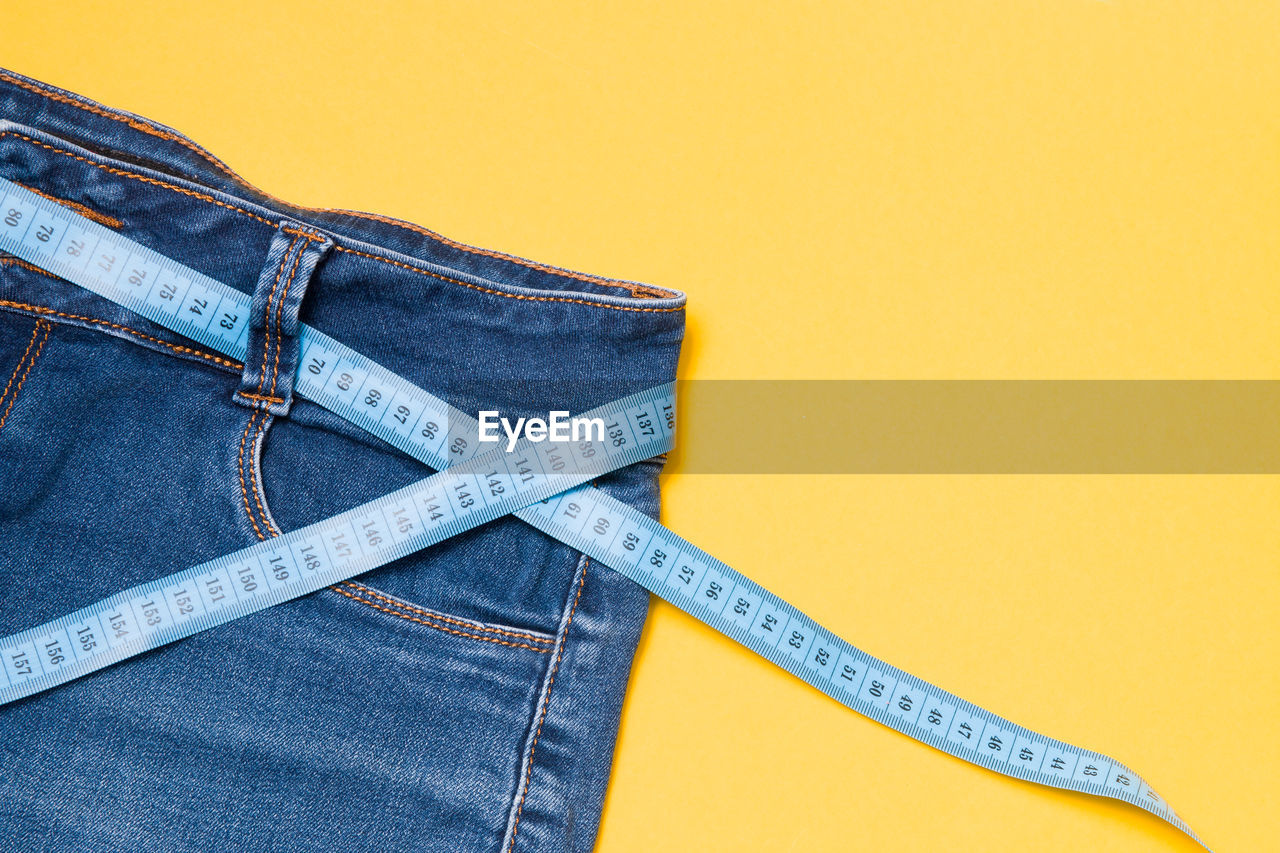 Close-up of jeans with tape measures over colored background