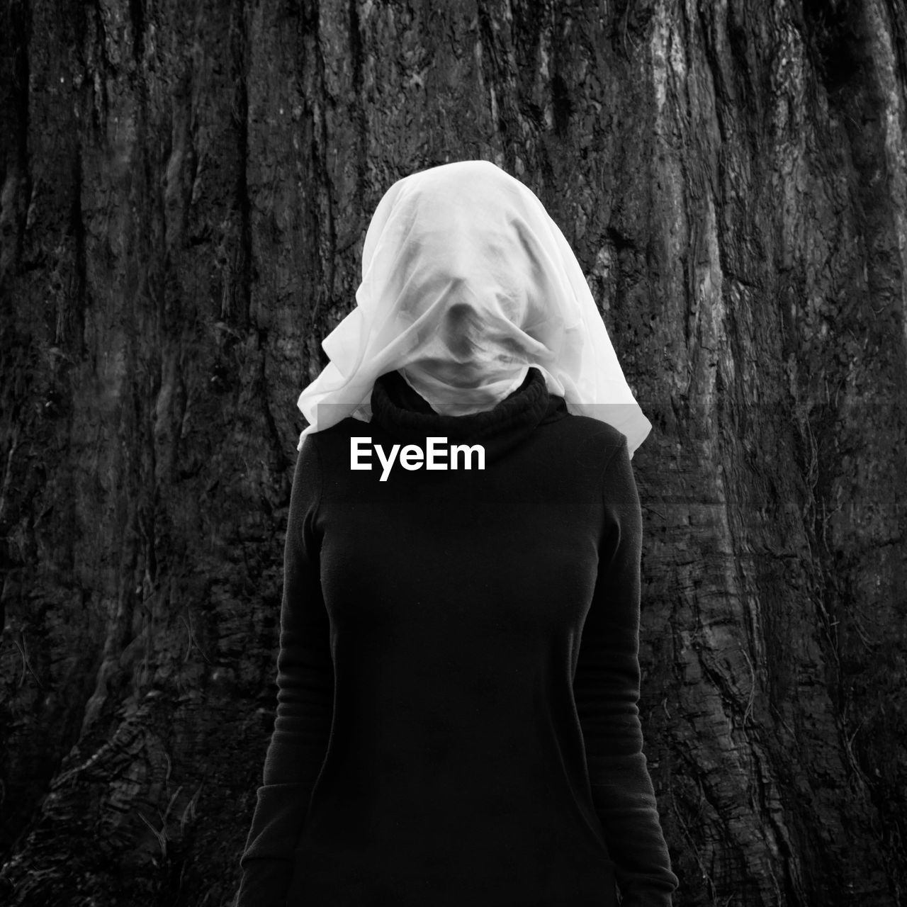 Woman with face covered standing against tree trunk 