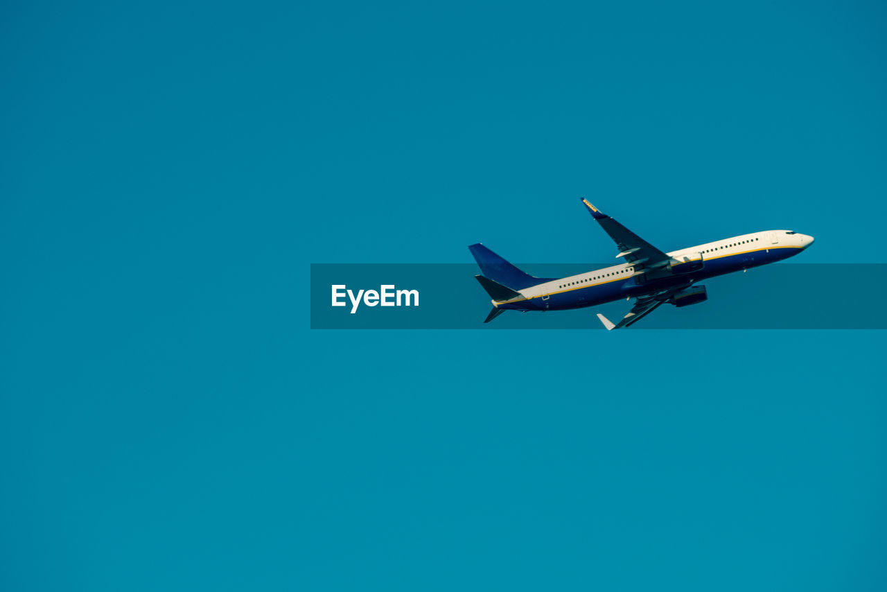 LOW ANGLE VIEW OF AIRPLANE FLYING IN CLEAR BLUE SKY