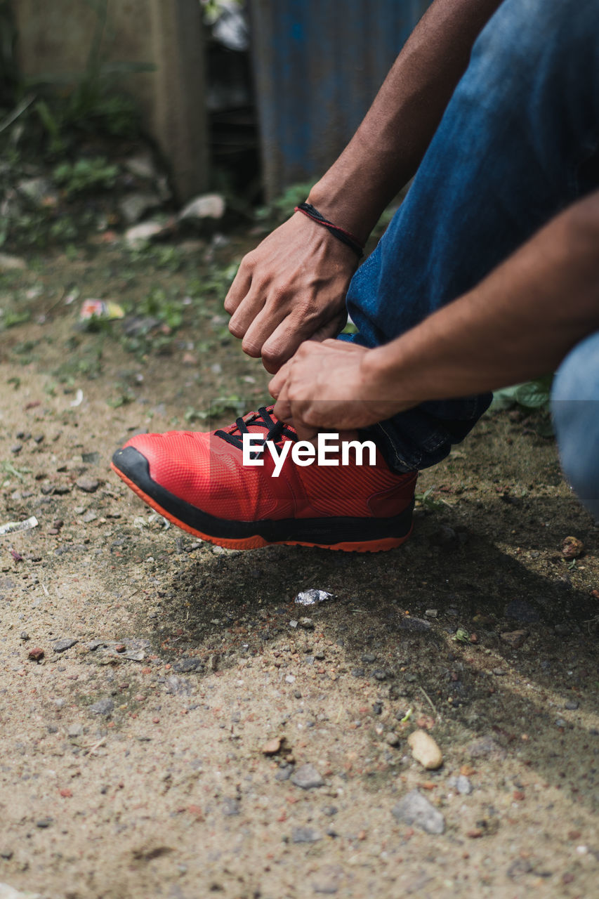 Low section of man tying shoelace while sitting on field