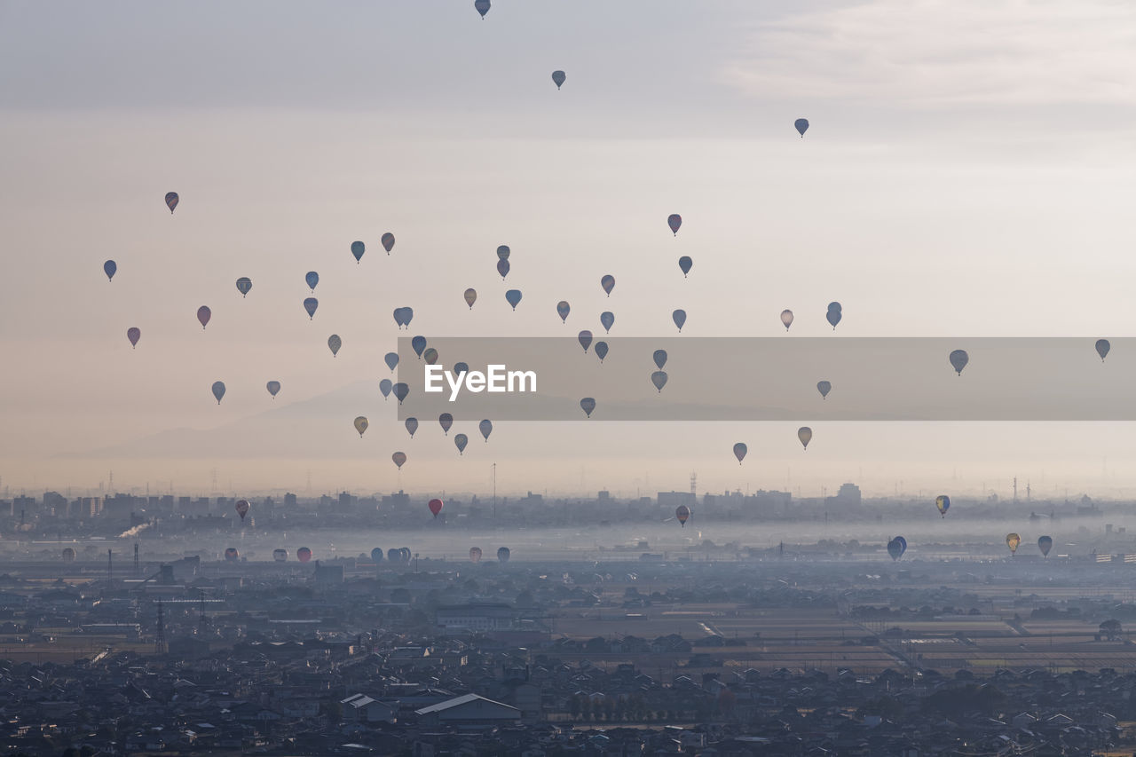 Flock of hot air balloons flying in city against sky