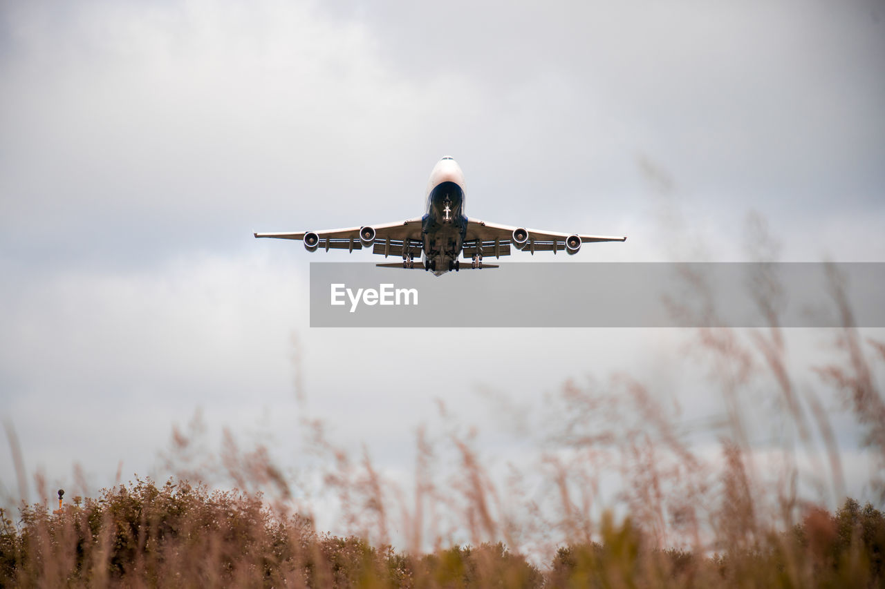 LOW ANGLE VIEW OF AIRPLANE FLYING AGAINST CLOUDY SKY