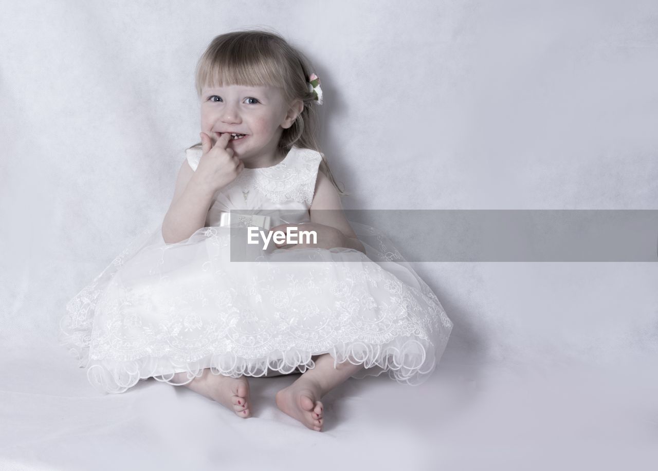 Portrait of cute little girl in white dress sitting on white background