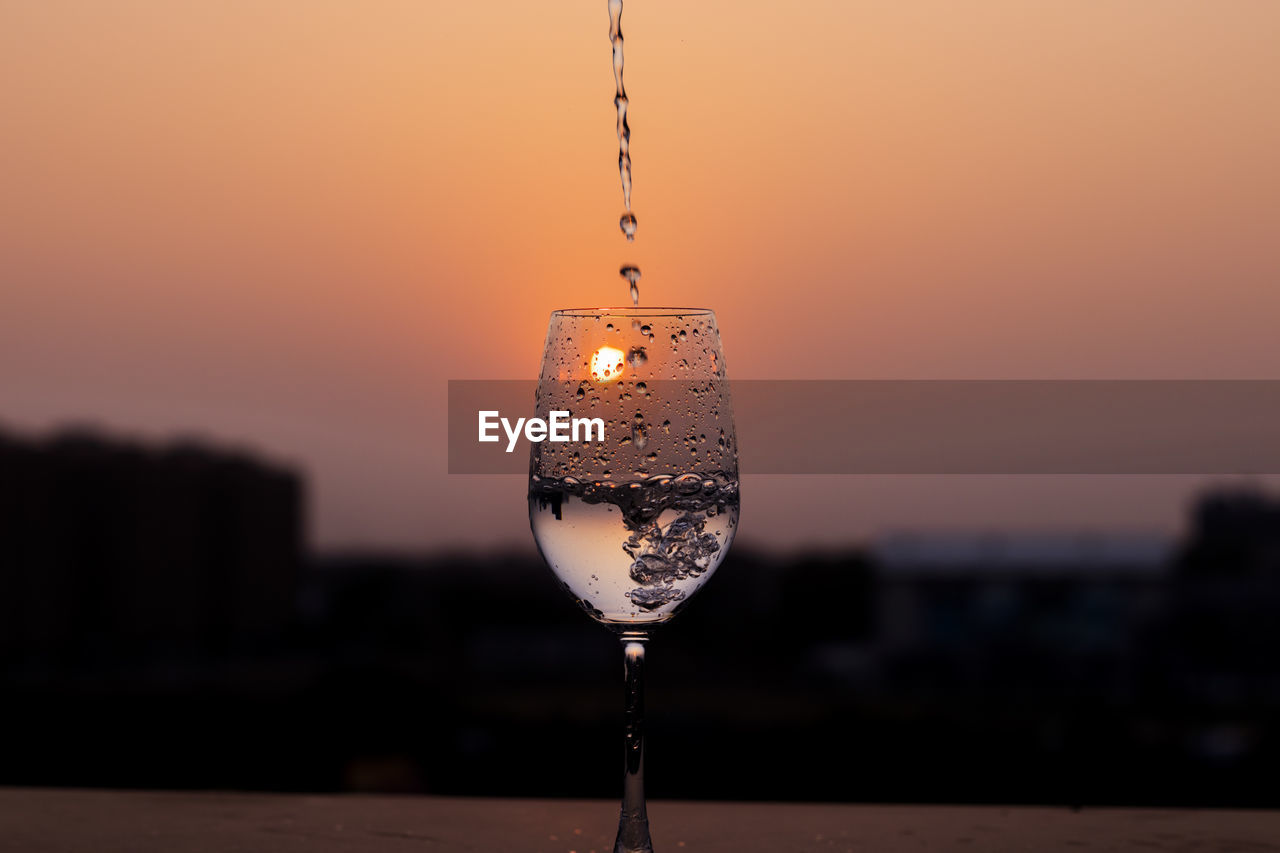 Clear liquid being poured into a wine glass at sunset