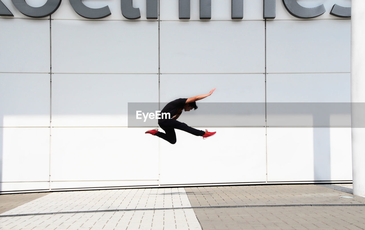 Man jumping on street against wall