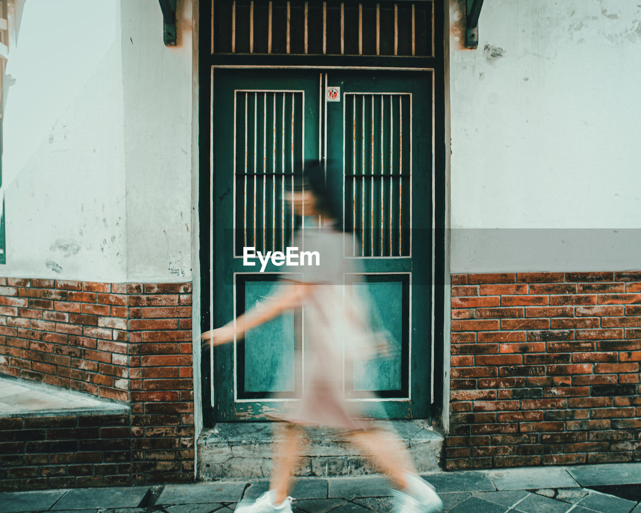 Blurred motion of woman walking against building