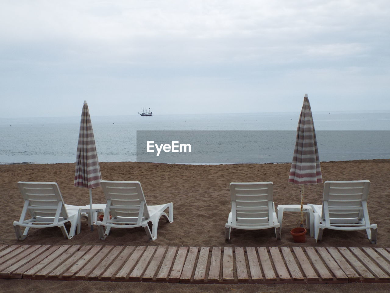 Lounge chairs with umbrellas at beach against cloudy sky