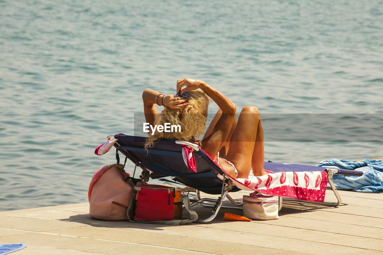 Close-up of woman sitting on lounge chair on pier by sea