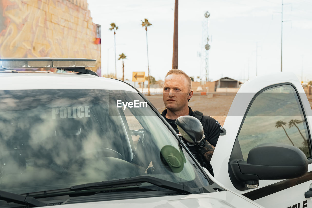 Horizontal image of white male caucasian police officer standing in the door opening of his trooper 