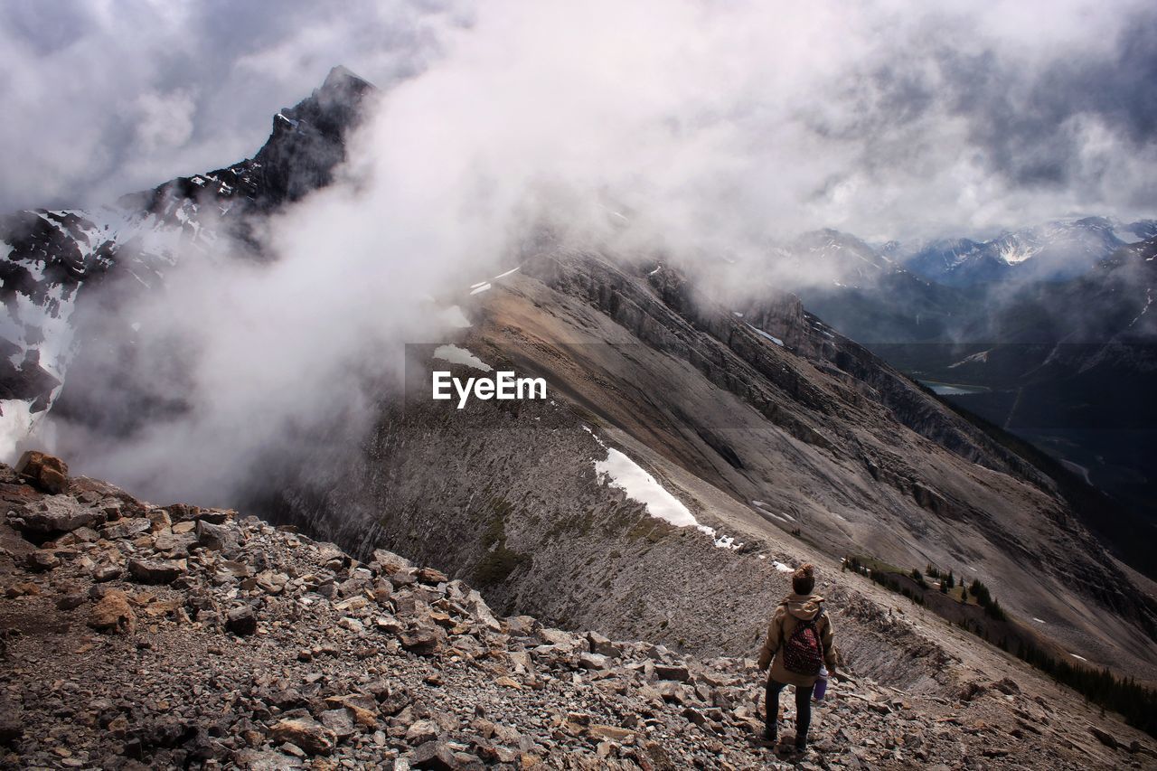 Scenic view of hiker and cloud covered mountains against sky