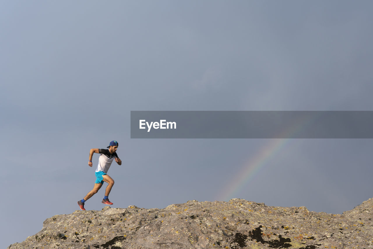 One man trail running on a rocky terrain with a rainbow