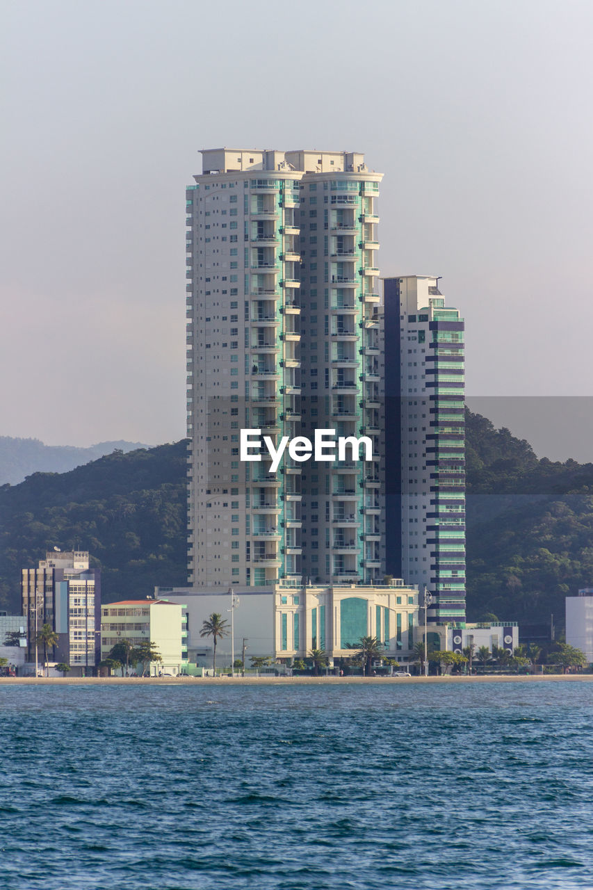 SEA BY MODERN BUILDINGS AGAINST SKY IN CITY