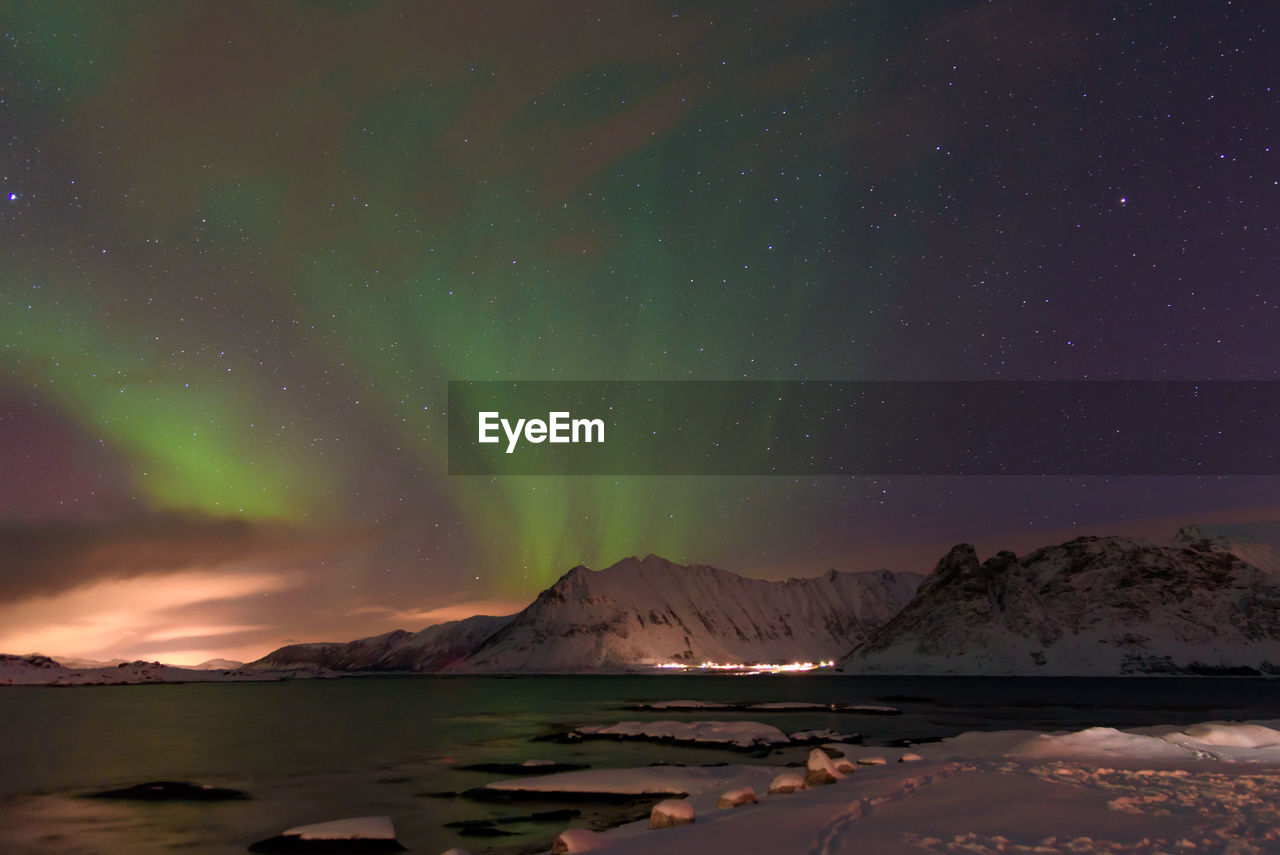 Scenic view of lake by snowcapped mountains against sky at night