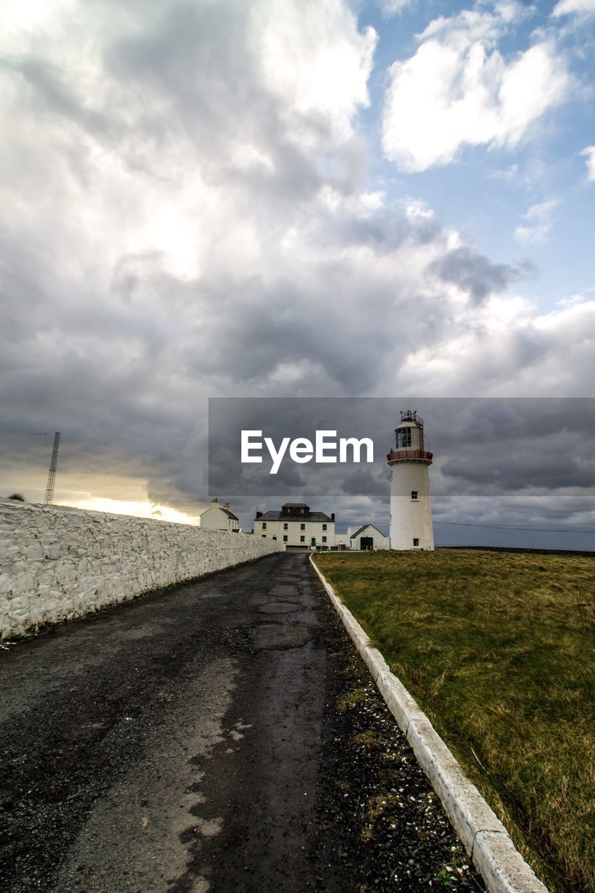 Road leading towards lighthouse amidst buildings against sky