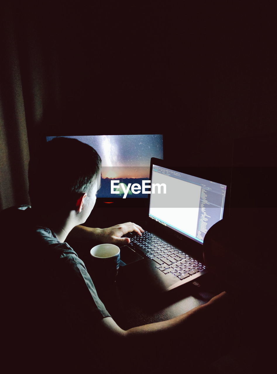 High angle view of man using laptop on table in darkroom