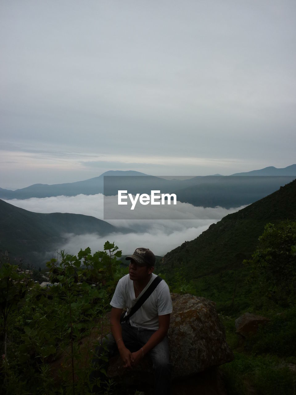 High angle view of young man sitting on rock against sky