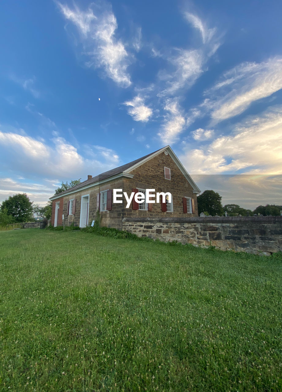 architecture, sky, built structure, grass, cloud, building exterior, rural area, building, plant, house, nature, field, landscape, lawn, green, farm, meadow, land, no people, residential district, rural scene, hill, environment, prairie, estate, home, grassland, outdoors, blue, barn, beauty in nature, history, pasture, scenics - nature, mansion, front or back yard, agriculture, the past, agricultural building, tree, sunlight, plain