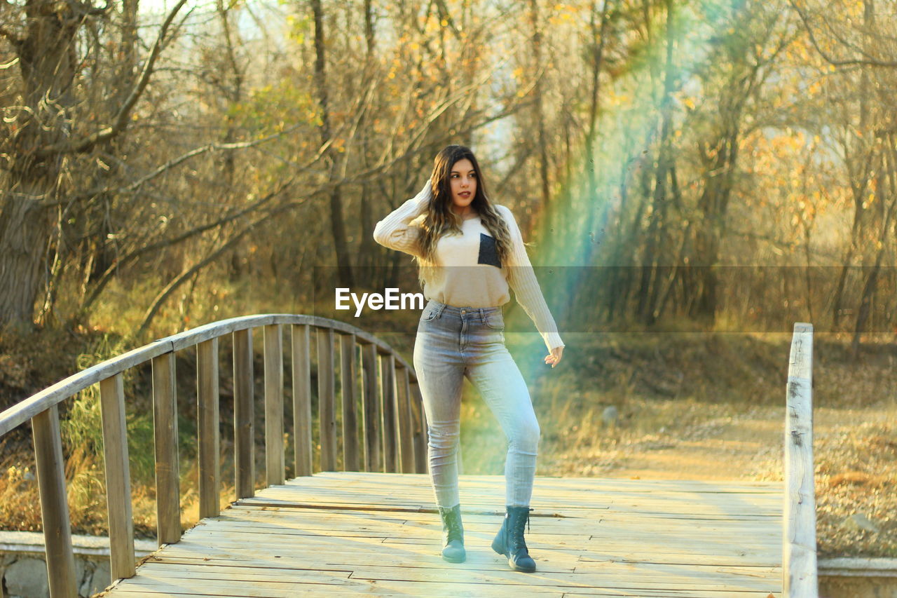 Young woman standing on footbridge at forest during autumn