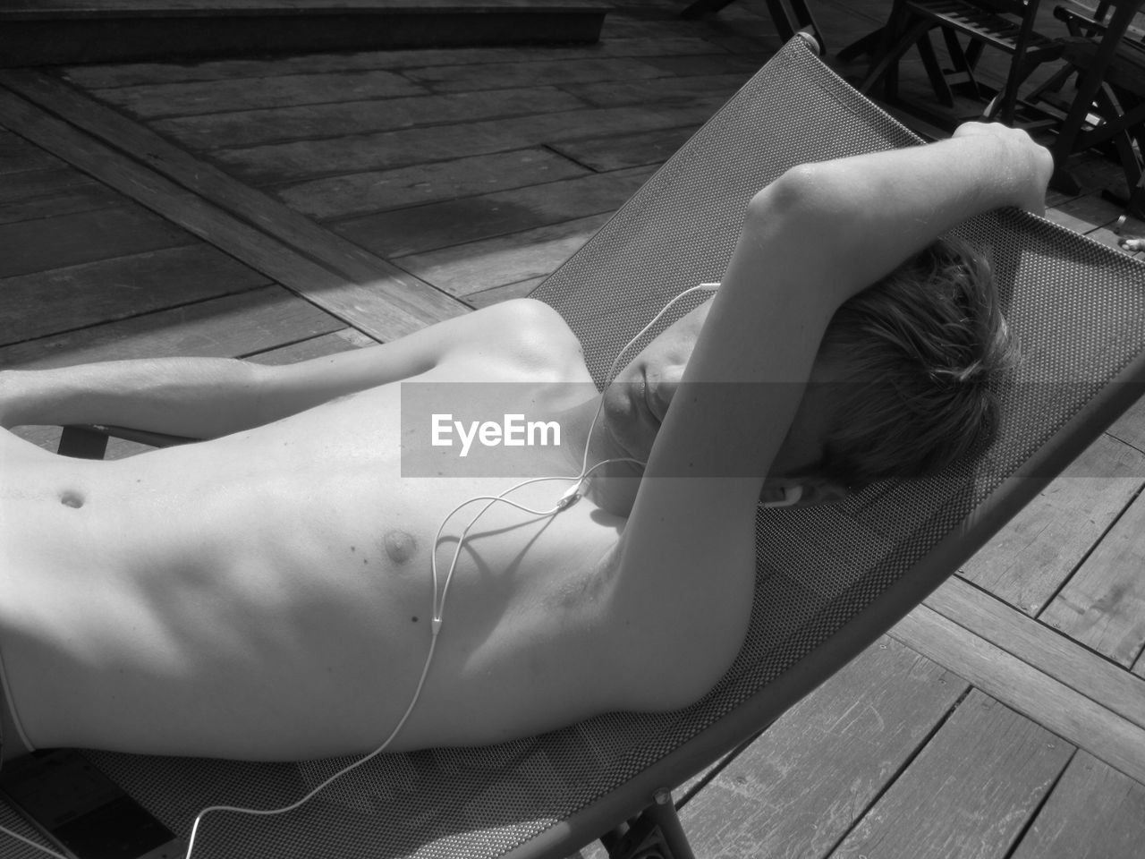 Shirtless teenage boy listening to music on headphones while lying on deck chair