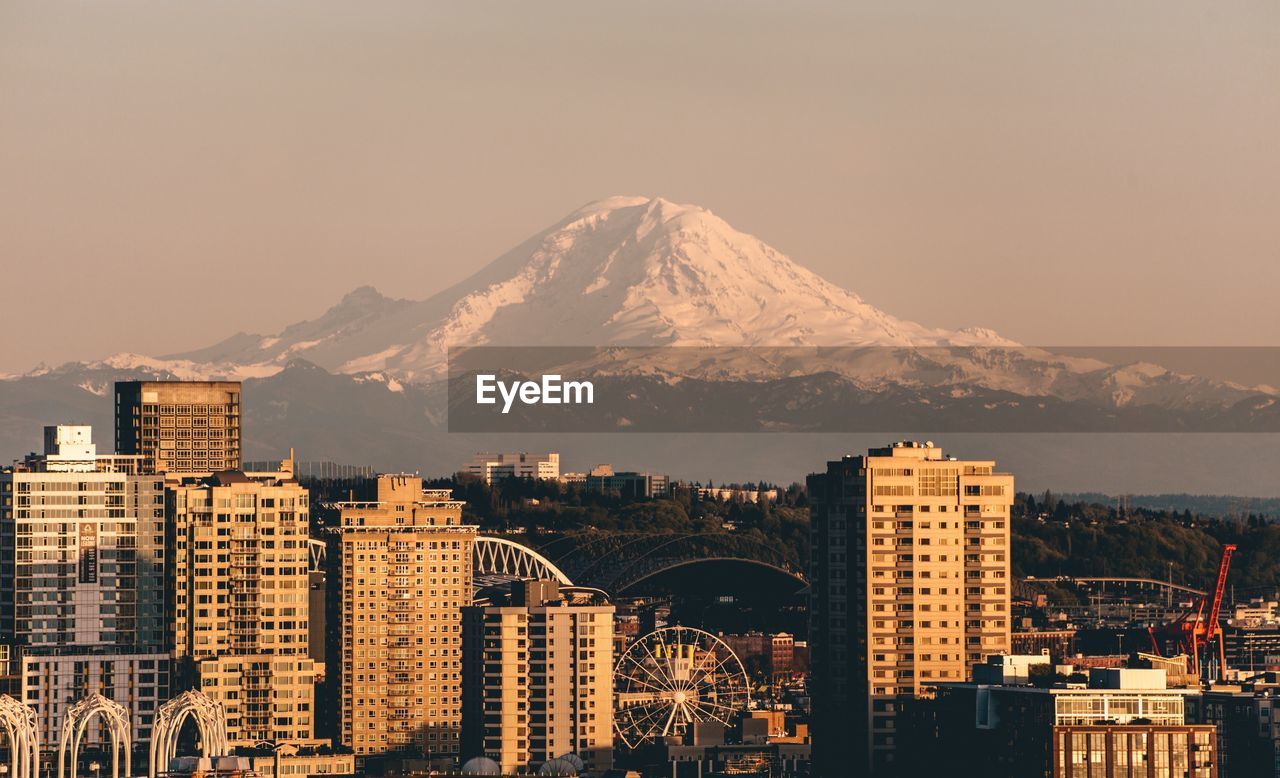 Buildings by snowcapped mountain against sky during sunset