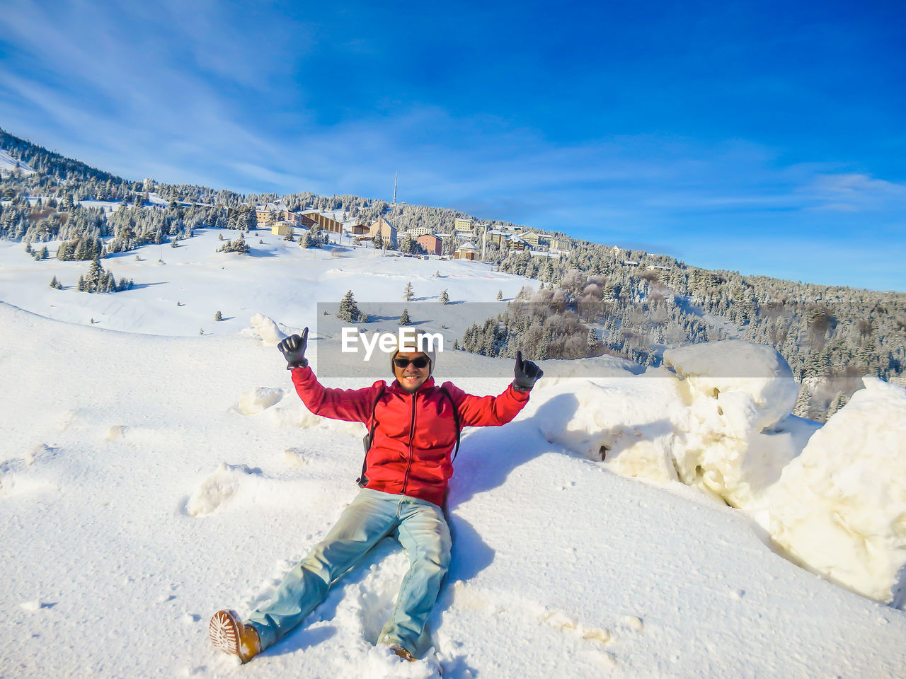 Portrait of man showing thumbs up while sitting on snowcapped mountain against sky