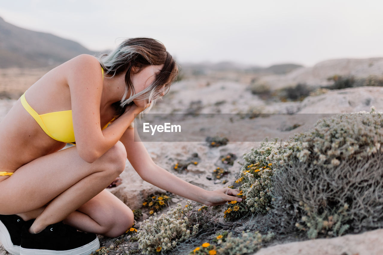 Carefree young woman touching flower while sitting on land