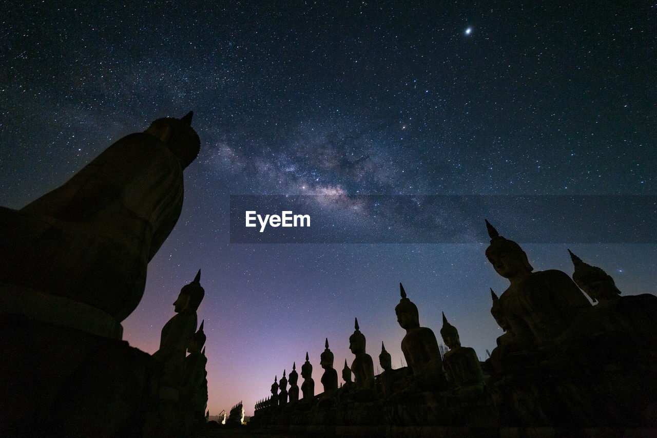 Low angle view of buddha statues against star field at night