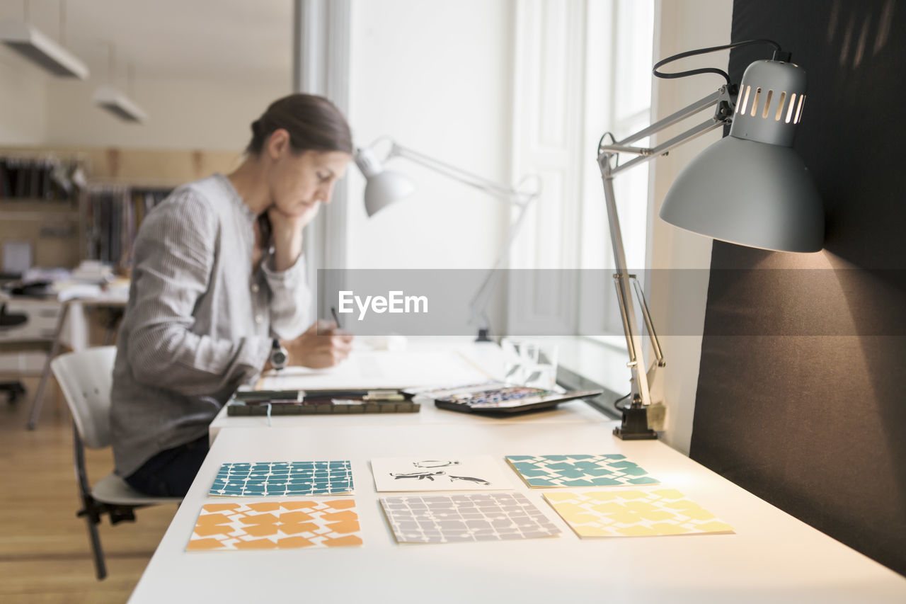 Woman painting on canvas by illuminated desk lamp at creative office