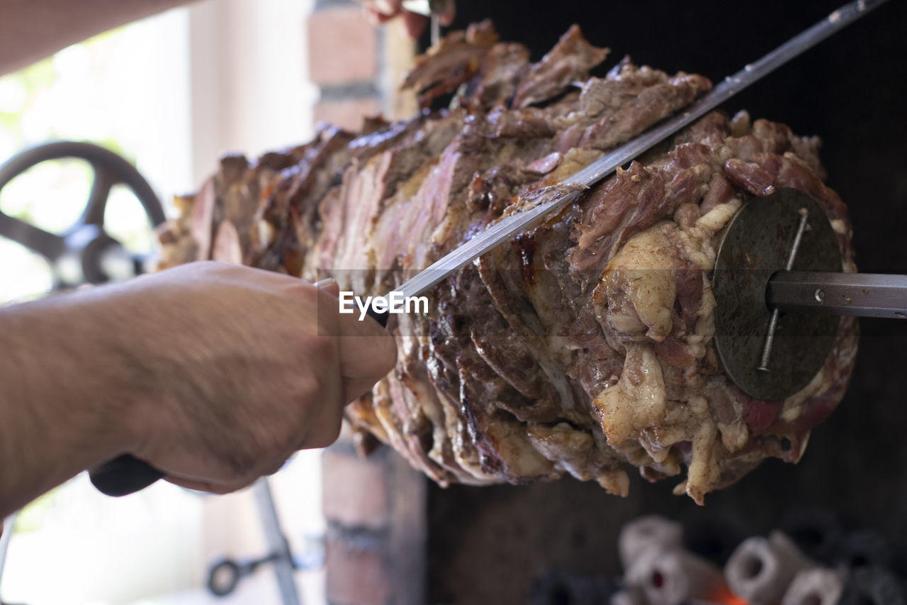 Close-up of man slicing meat from skewer at store