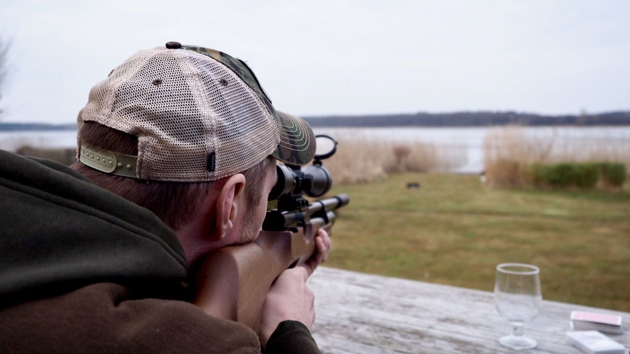Close-up of man aiming with rifle against lake