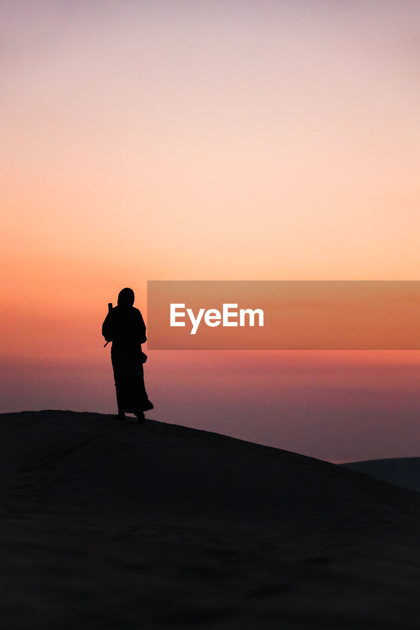 Silhouette woman standing on shore against sky during sunset