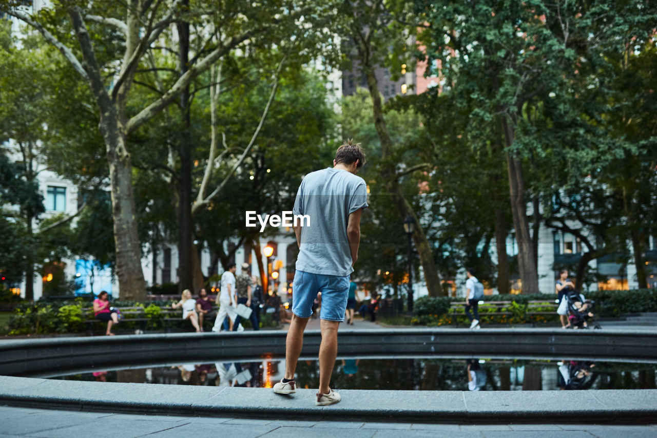 Rear view of young man standing by pond in city