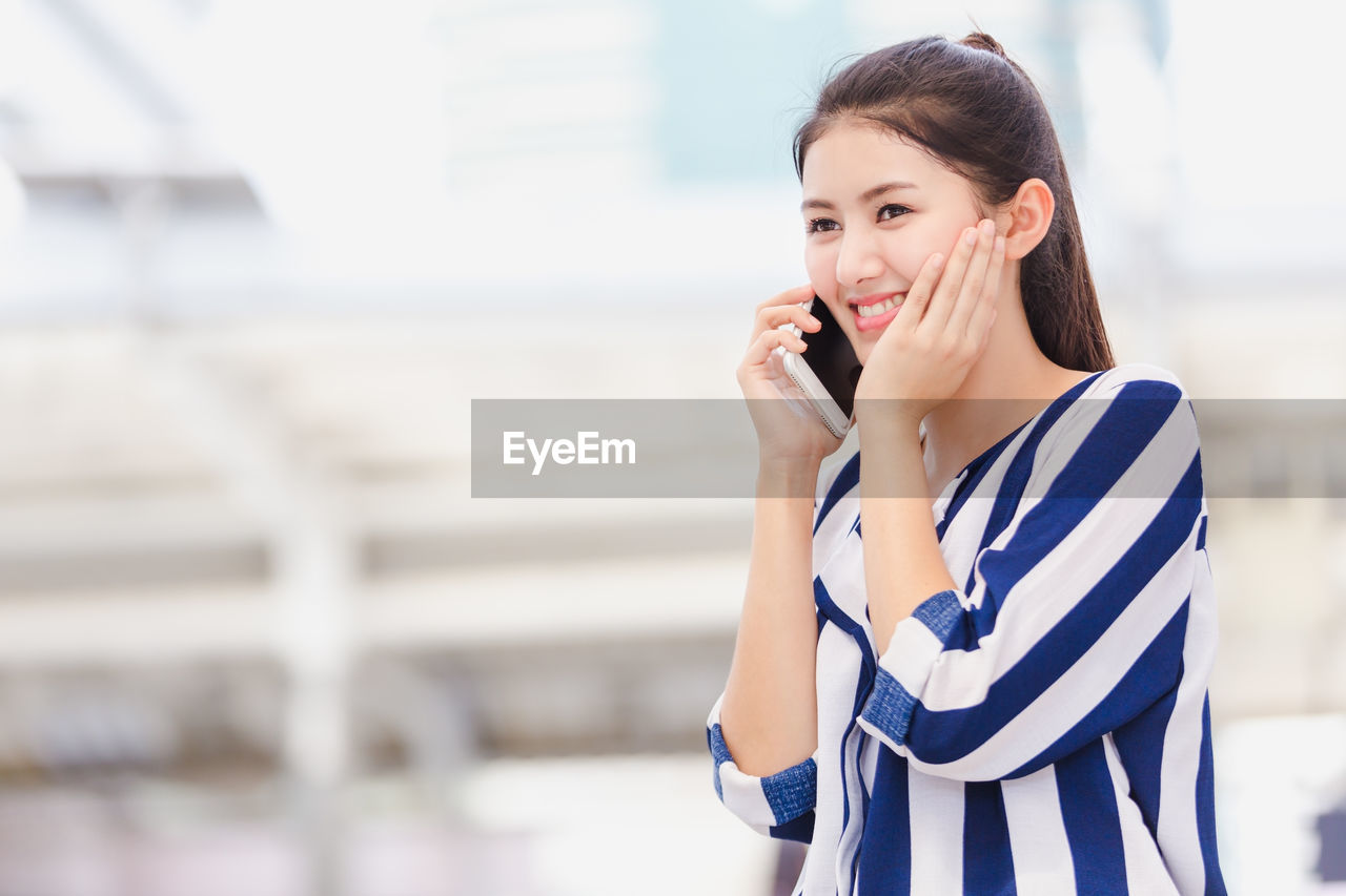 Young woman talking on mobile phone while standing outdoors