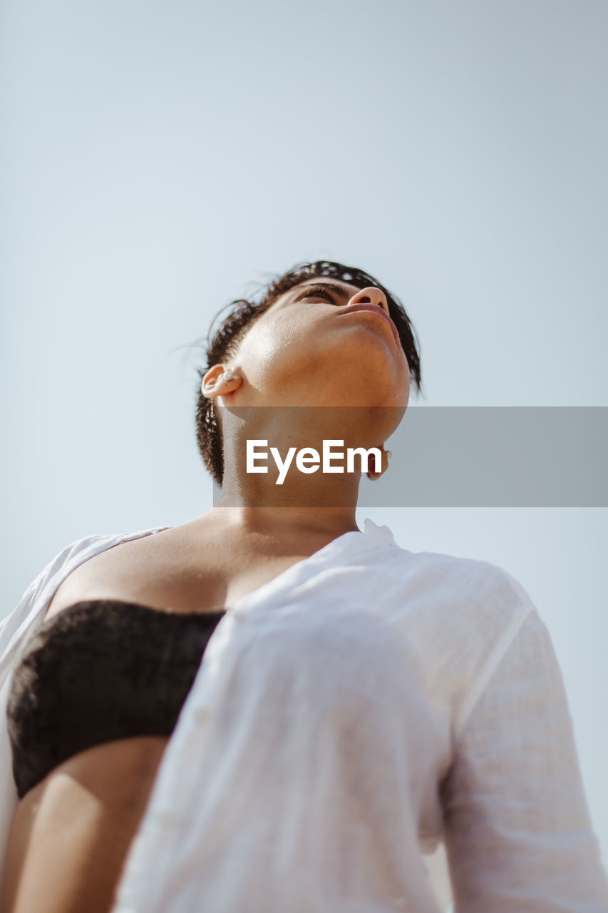 LOW ANGLE VIEW OF YOUNG MAN LOOKING AT CAMERA AGAINST SKY