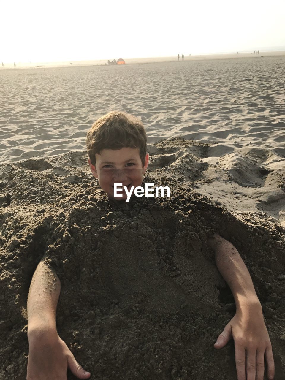 Portrait of smiling boy buried in sand at beach