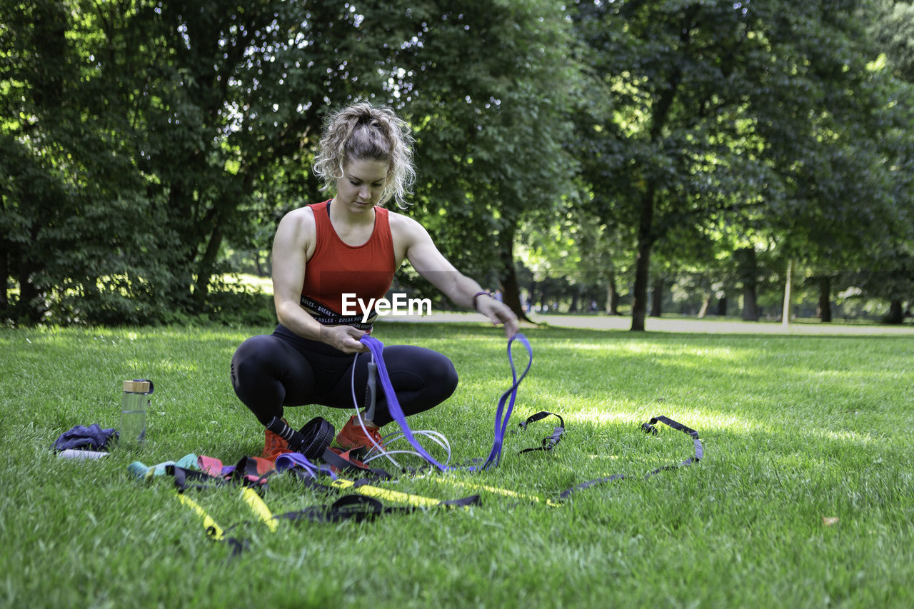 A young blond female cross fit athlete organises her fitness equipment in a park.