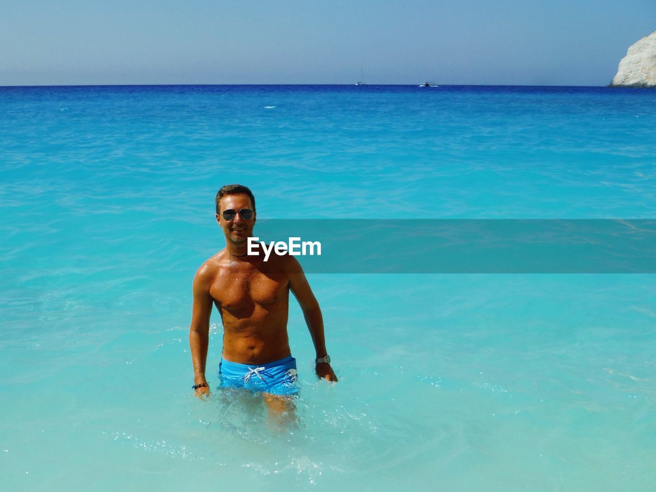 Portrait of shirtless man standing in sea against sky on sunny day