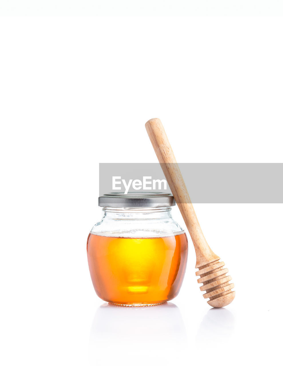 Honey in closed lid glass jar with wooden honey dipper leaning on its side