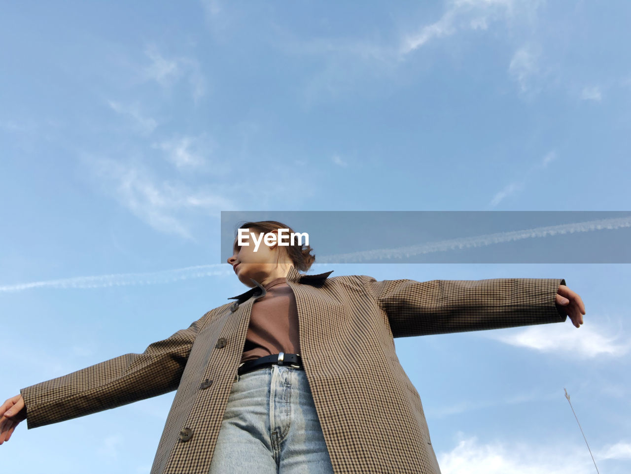 Low angle view of young woman looking away against sky