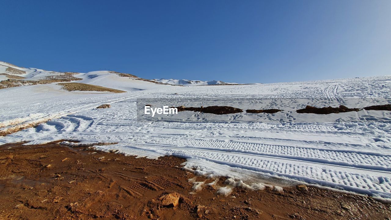 Snow covered landscape against clear blue sky