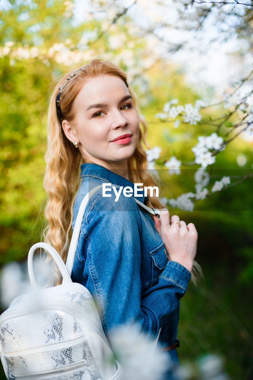 Smiling young woman standing against trees