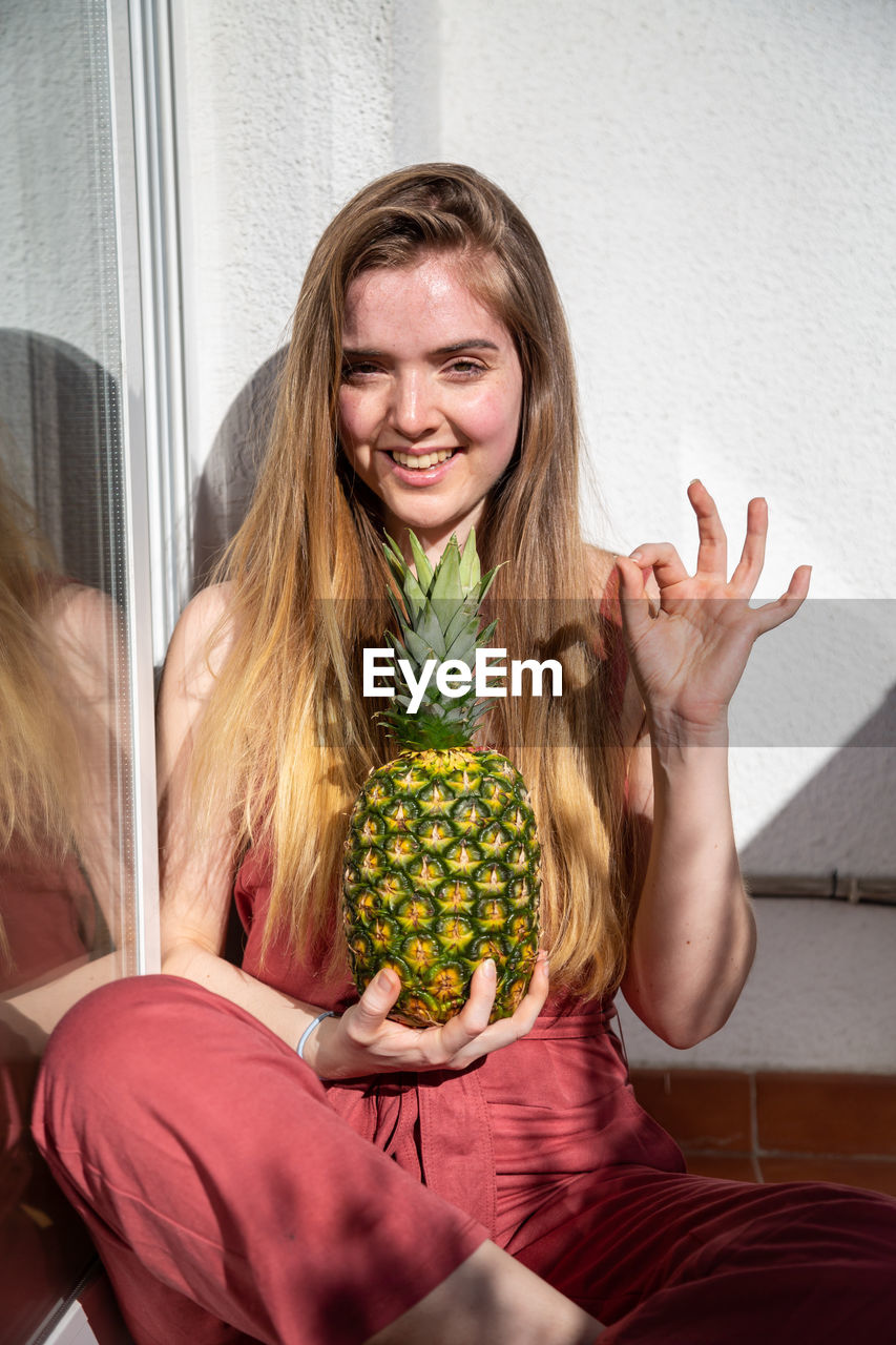 PORTRAIT OF A SMILING YOUNG WOMAN WITH FRUITS IN BACKGROUND