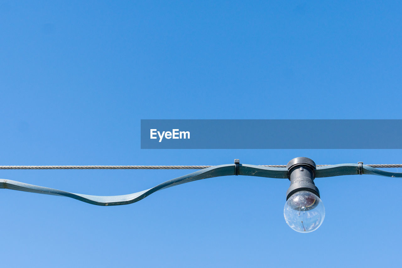 Light bulb hanging on wire against clear blue sky