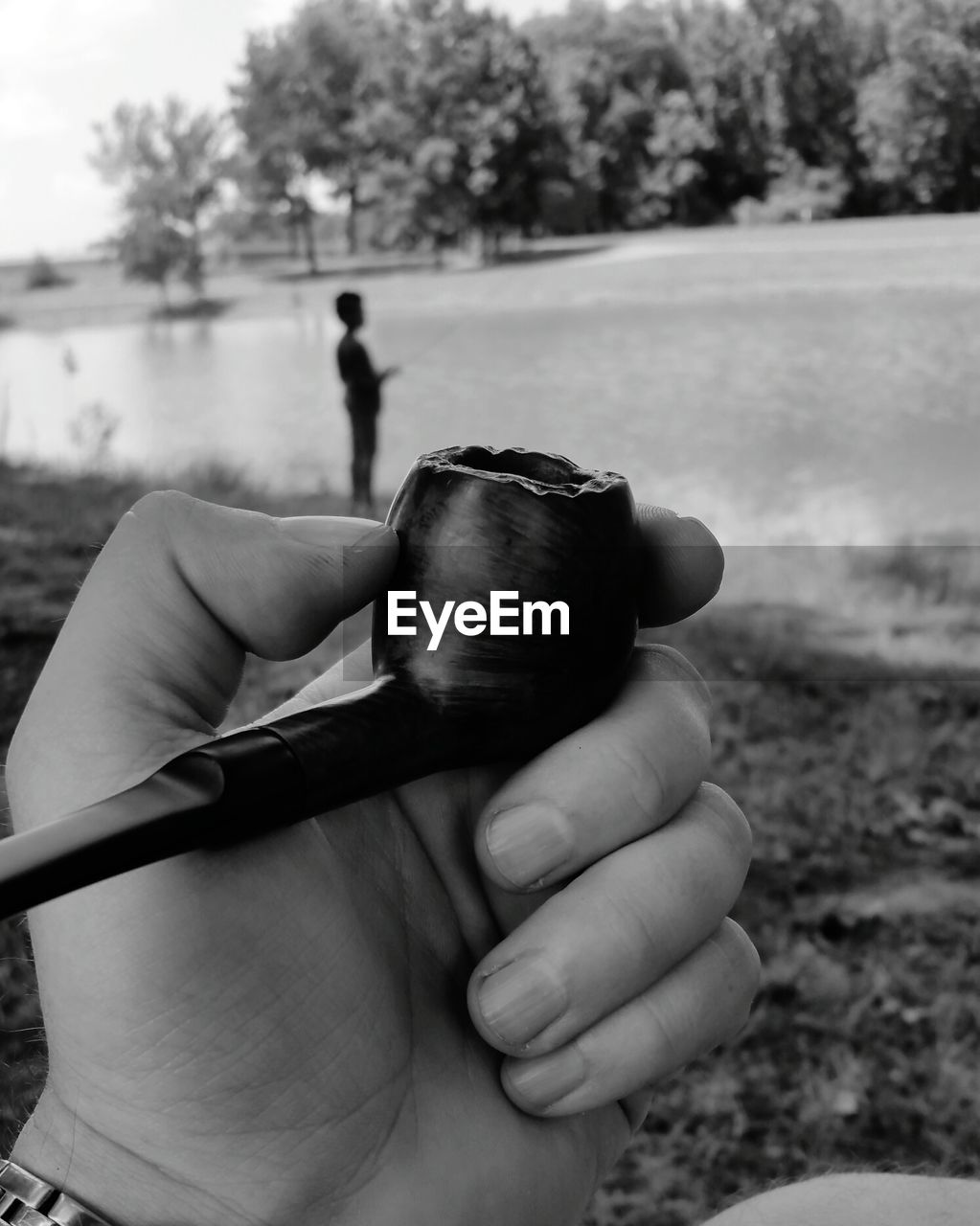 Cropped image of person holding smoking pipe against river