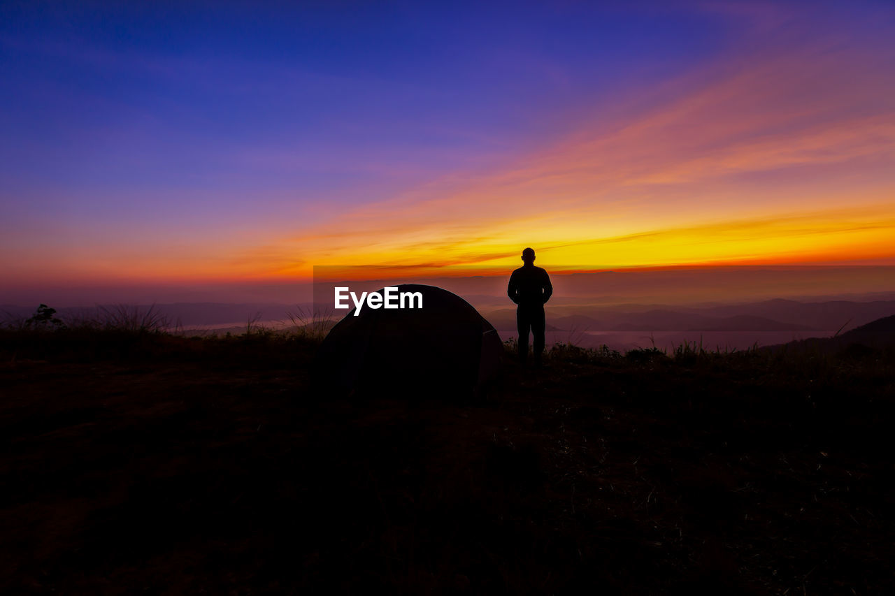 SILHOUETTE MAN STANDING ON FIELD AT SUNSET