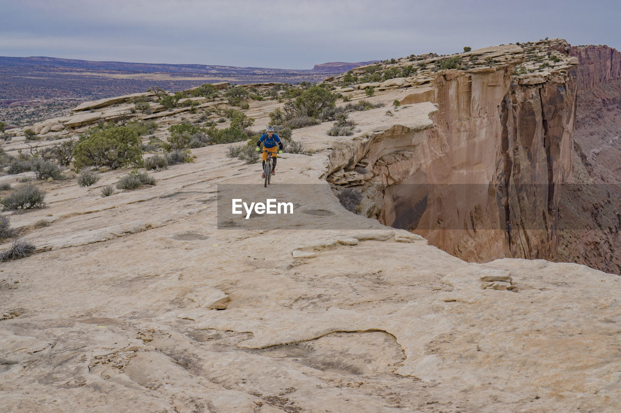 Man cycling on cliff against sky