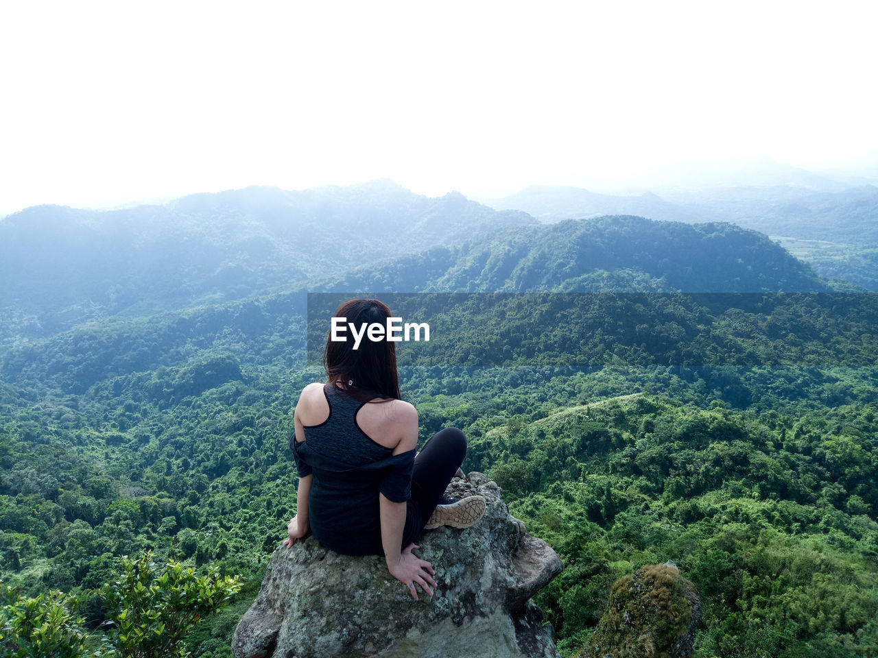 Rear view of woman sitting on rock against landscape