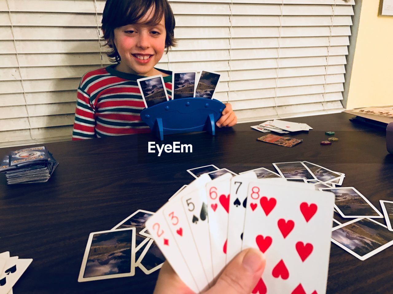 Boy playing cards with person on table