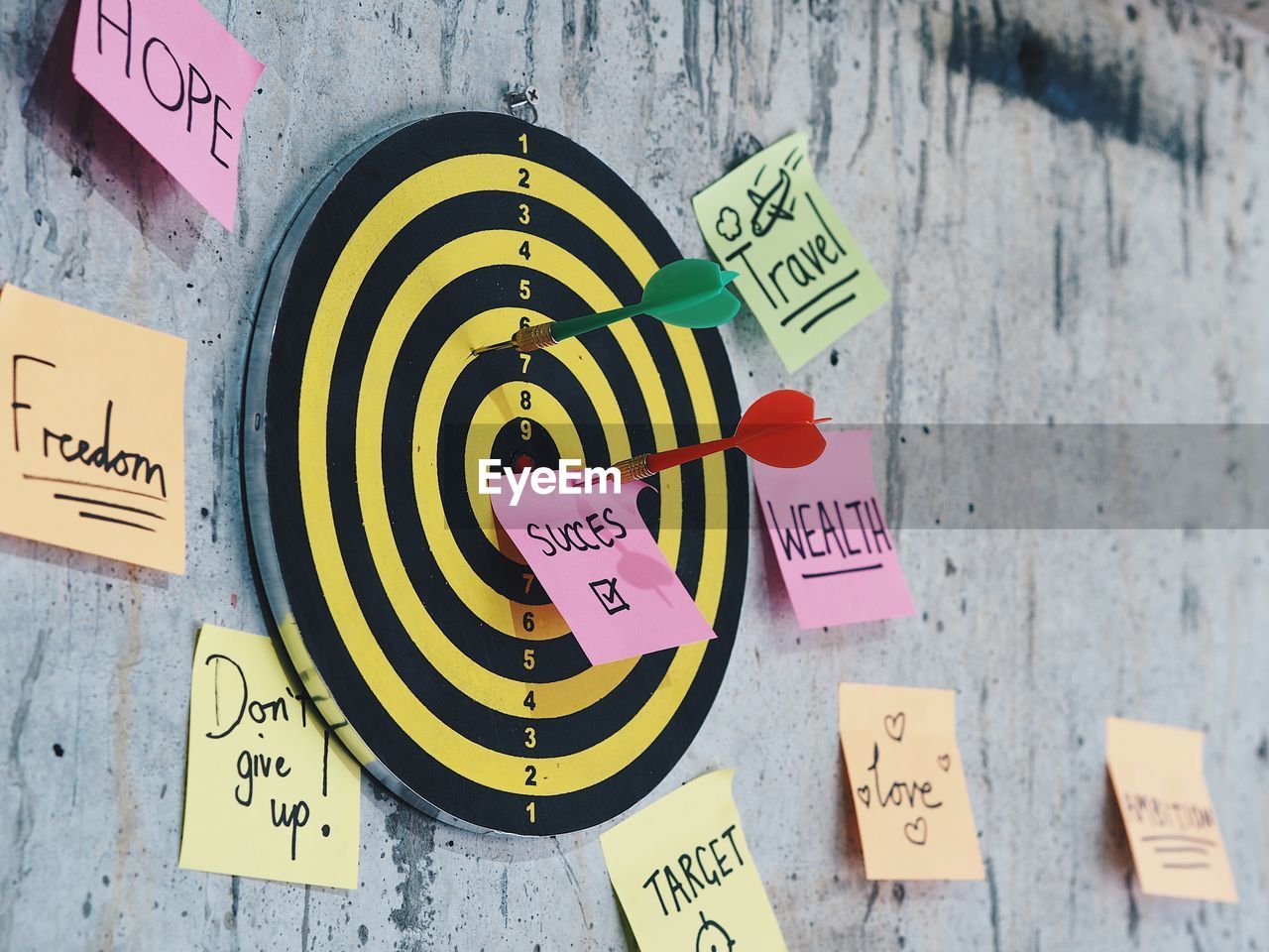 Close-up of dart on dartboard with adhesive notes against wall